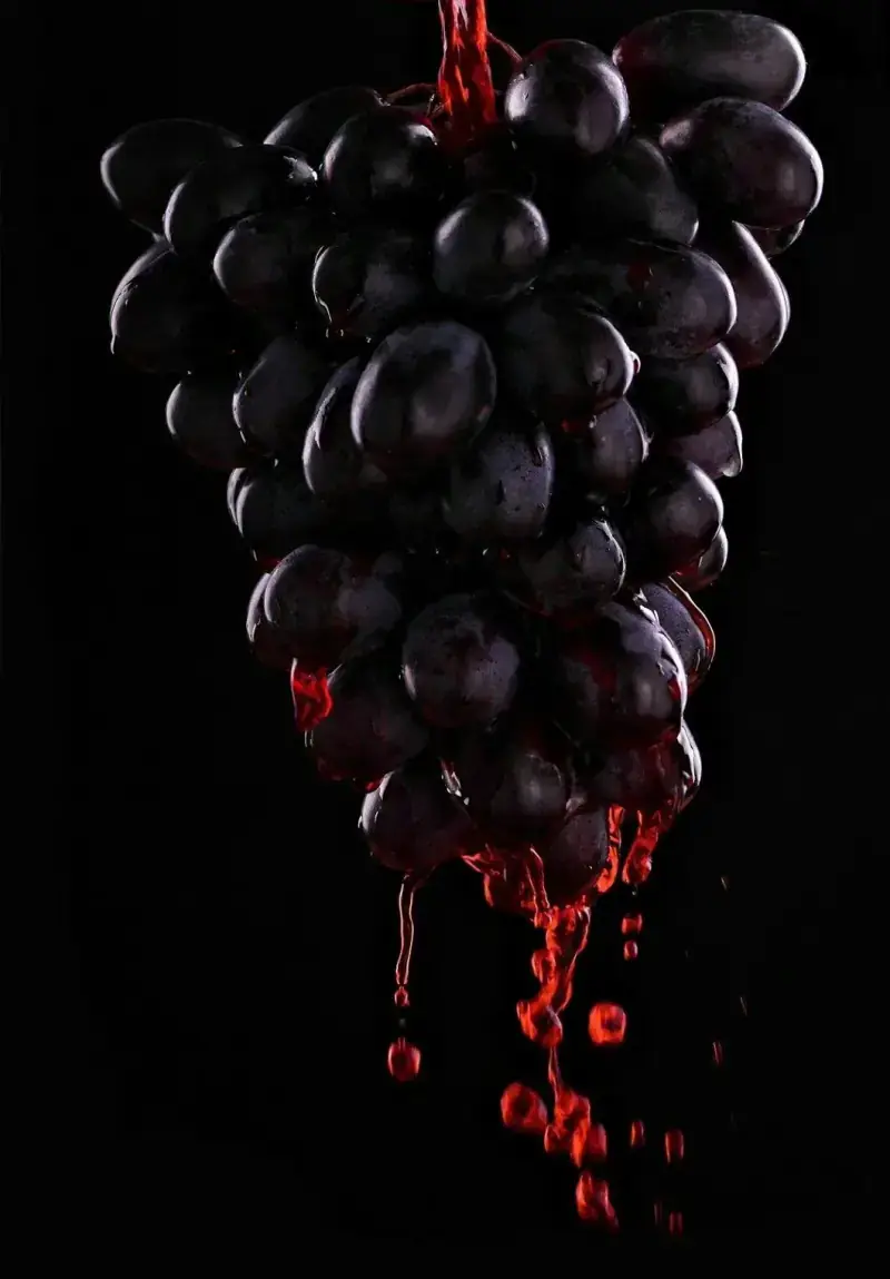 A bunch of black grapes with wine running from them